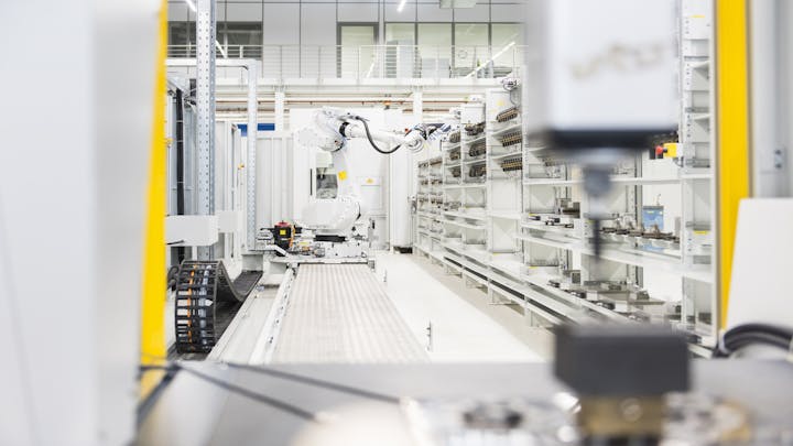 Spezialist für Qualitätskontrolle, der QMS-Software auf einem Tablet in der industriellen Umgebung mit Roboterarmen einsetzt.