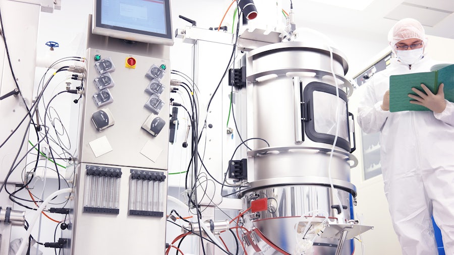 A scientist looking at notes next to a bioreactor.