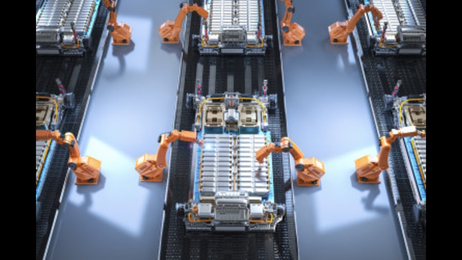 An overhead look of a factory floor with a row of robotic arms assembling next generation electric vehicles.