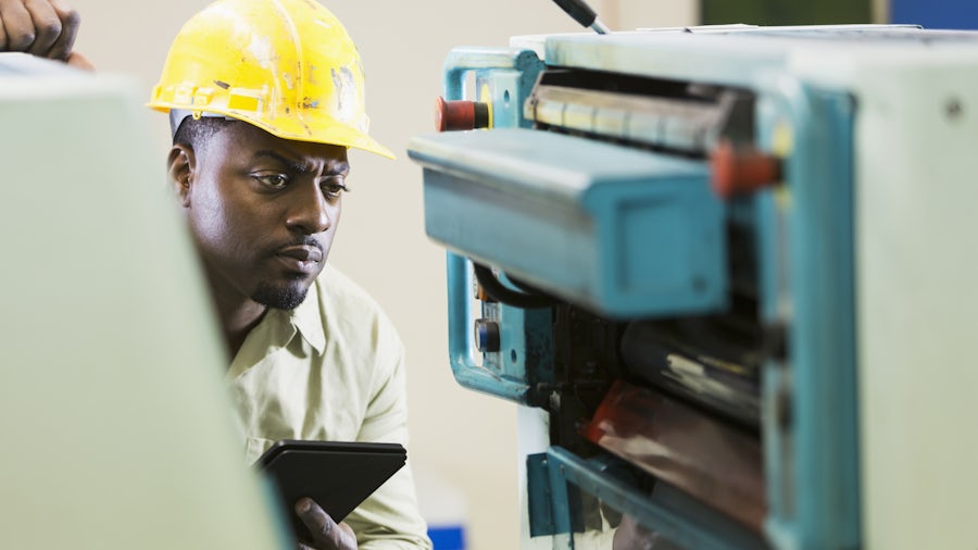 An engineer inspects an industrial machine with a tablet in his hand.