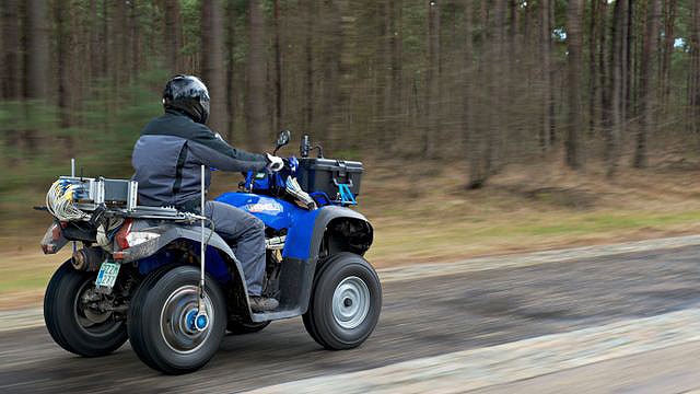 A man is riding a quad bike on a countryside road.