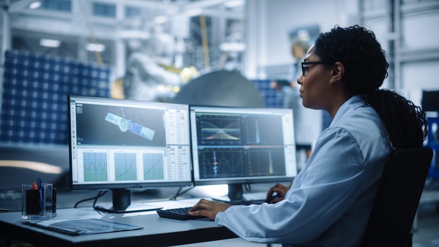 A worker sitting at a desk looking at an image of a satellite and its testing data on a computer monitor