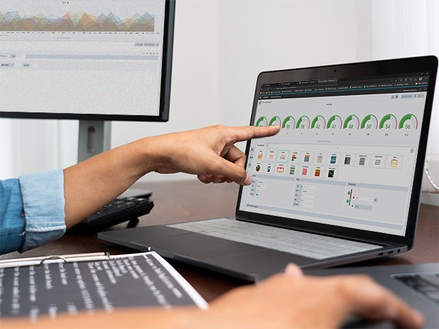 A person's arm pointing at a laptop screen displaying charts.