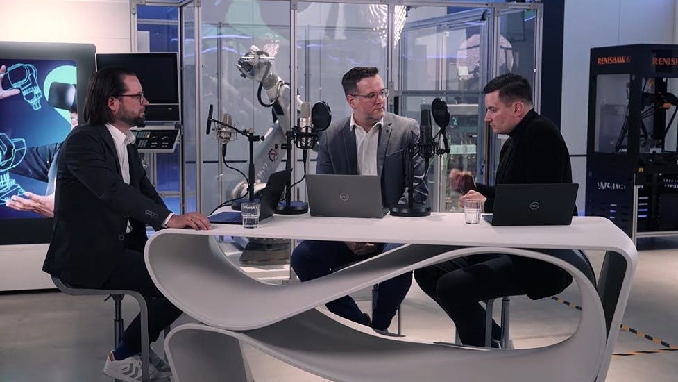 Geschäftsleute in Business-Kleidung führen ein Gespräch in einer modernen Technologie-Umgebung mit Renishaw-Ausrüstung, digitalen Bildschirmen und fortschrittlicher Messtechnik im Hintergrund.