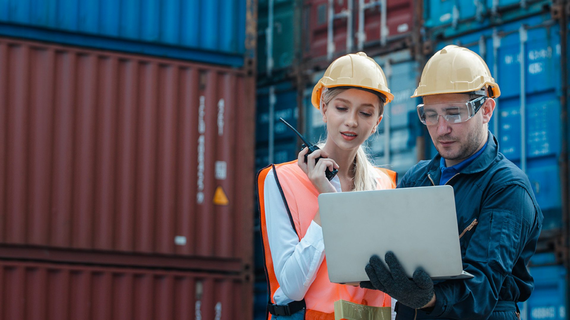 Two people working on a computer at a shipping container site.