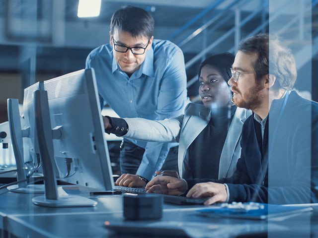 Three electronics development engineers working on a computer during a discussion.