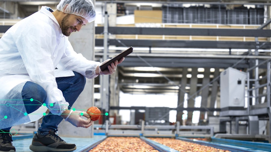 Factory worker holding a peach and a tablet by an assembly line