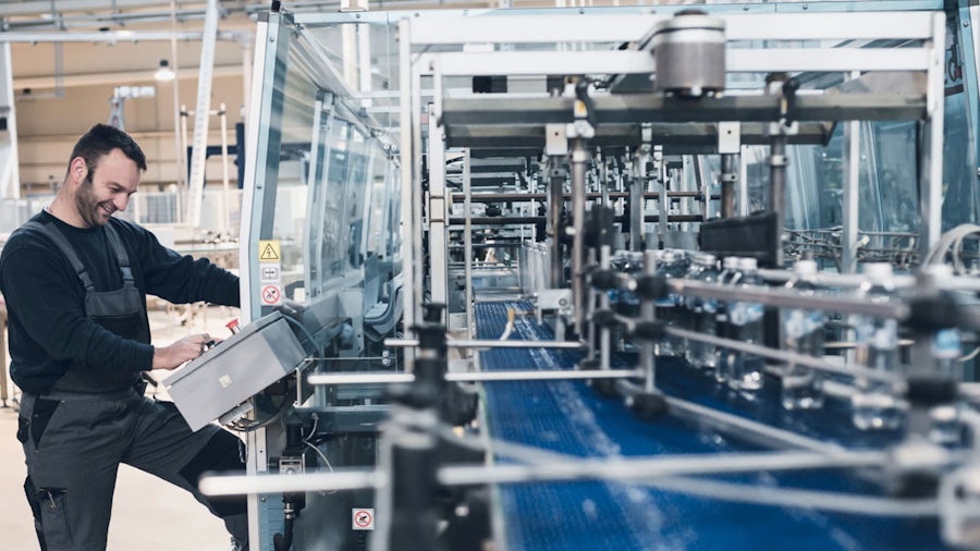 A worker in a food and beverage manufacturing facility operates a control panel on an automated production line, where bottled water is being processed. 