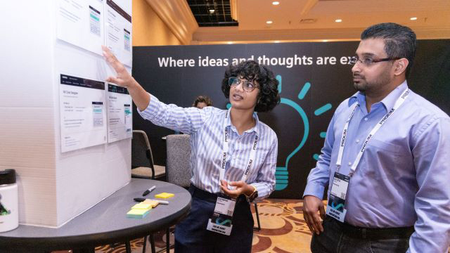 Woman pointing at a whiteboard of user interfaces to get feedback from another attendee at Realize LIVE.