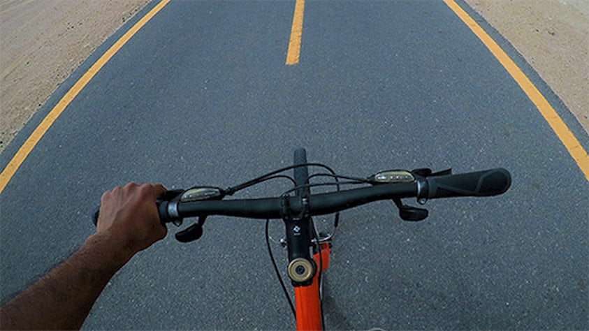 A hand holding a bike handle while riding on a road.