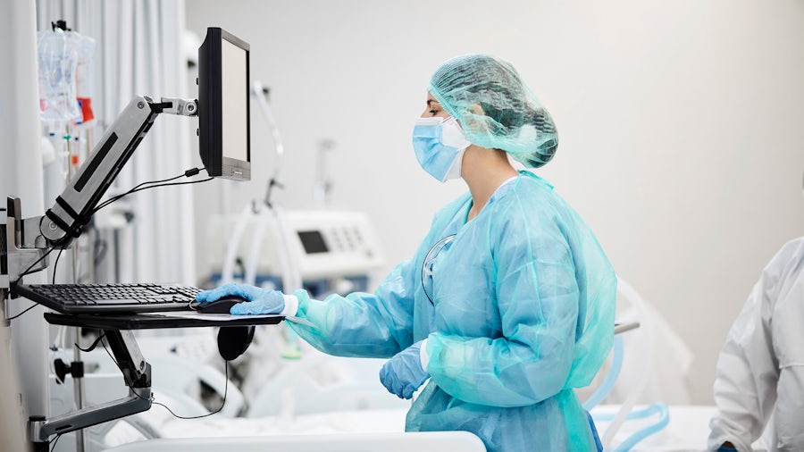 Medical professional wearing protective gear looking at a computer monitor in a hospital room conducting design control for medical devices.