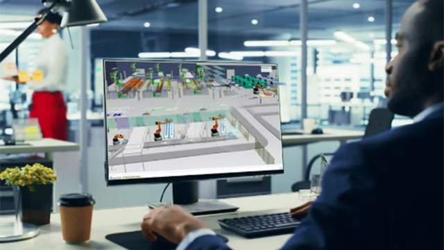 A man works on a computer displaying a mock-up of a factory floor