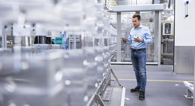 Man in jeans in a manufacturing plant looking at a tablet