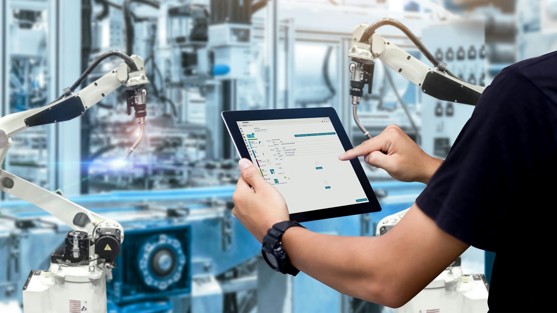 Hands holding a tablet with Siemens software with blurred automation machines in the background.