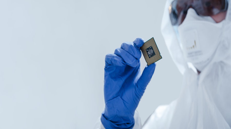 An engineer in a lab coat wearing gloves and protective eyewear looking at a microchip