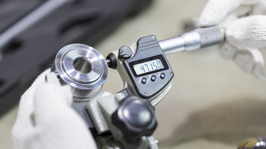 Manufacturing working using a gage to check the quality of a component. 