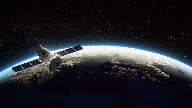 A satellite is shown orbiting earth with may stars shining in the dark backdrop of space. 