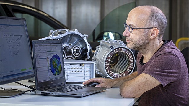 Inżynier korzystający z oprogramowania Simcenter na laptopie i różnych komponentów na stole do prognozowania osiągów NVH układu.