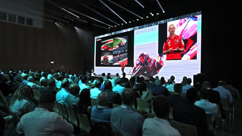 A speaker presents information and shows racing images to Realize LIVE Europe attendees.