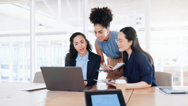 Three women working together on a computer.