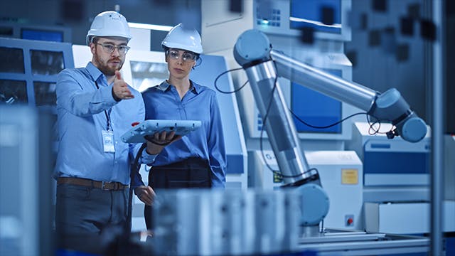 Male and female engineers use industrial digital tablet to work with a robotic arm for production line.