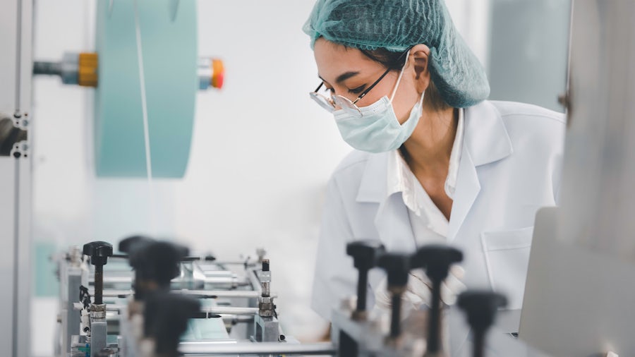 Doctor wearing a hair net and face mask as she looks at a medical device