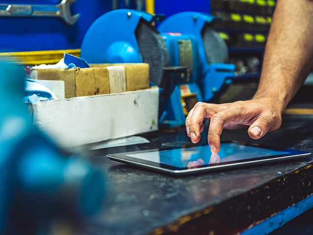 A tablet on a table in a machine shop, being accessing by a worker's hand