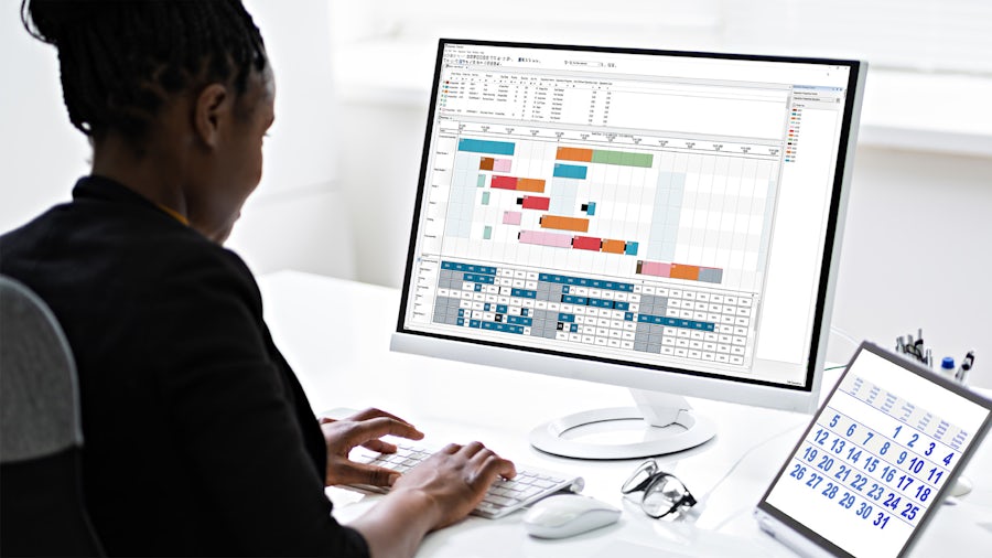 “Person using APS software on a computer for production planning and scheduling, with a calendar tablet nearby.