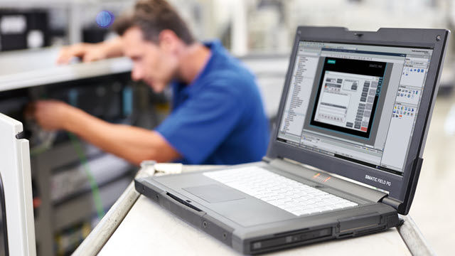 Engineer is fixing a FPGA in a machine and a laptop is showing the design 