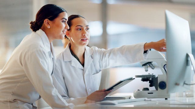 Two women wearing lab coats looking at a computer in a lab