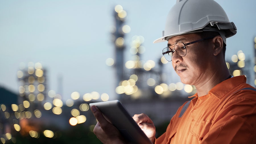 Man wearing a helmet using a tablet computer in front of a chemical site.