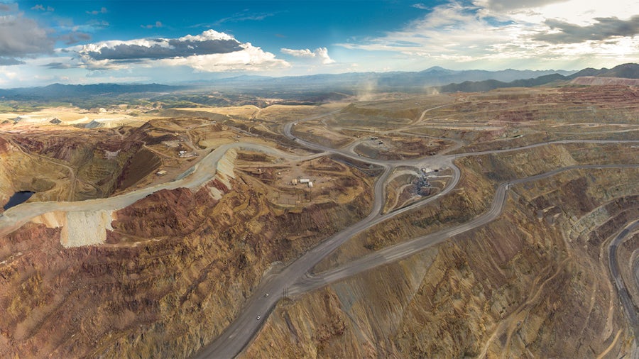 Aerial view of an open-pit mine, featuring terraced landscapes, roads, and distant mountains
