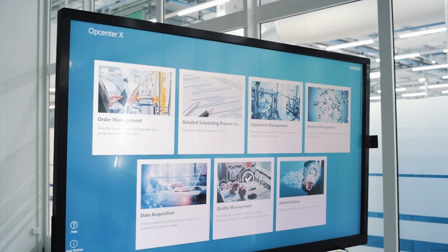 Nahaufnahme eines Computermonitors, auf dem Opcenter X läuft, mit einer Fertigungshalle im Hintergrund.