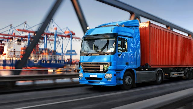 Blue truck with red container driving on a bridge