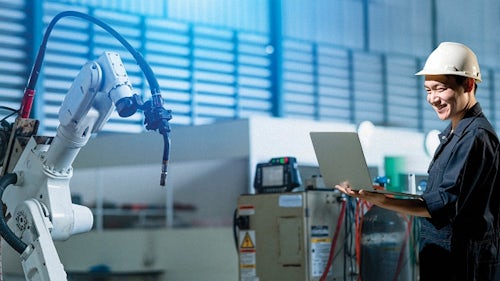 An engineering tech connects to an industrial robot arm to implement closed-loop manufacturing.