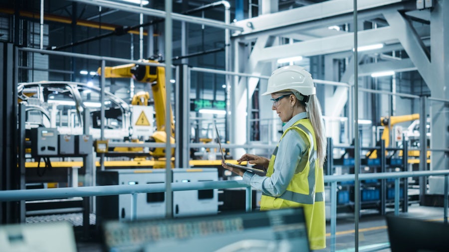 Projektleiter, der eine Montagelinie in der Automobilfertigung überwacht, während er Produktinformationen mit Hilfe einer PLM-Software auf einem Laptop überprüft.