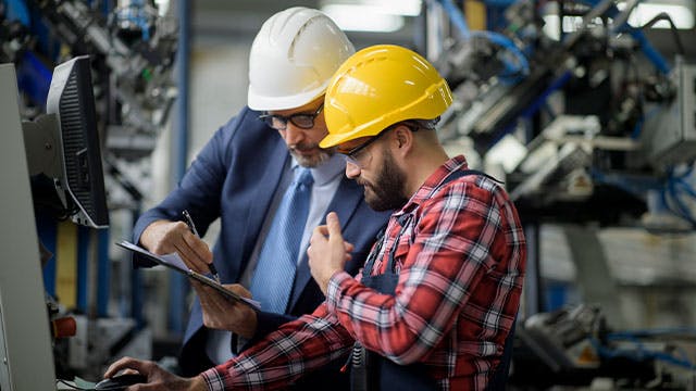 Dos trabajadores que consultan información en la planta de producción