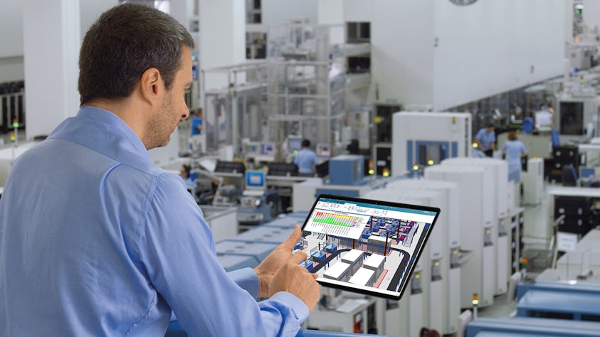 Male engineer reviewing a factory digital twin model in Tecnomatix Plant Simulation software on a tablet at the shop floor.