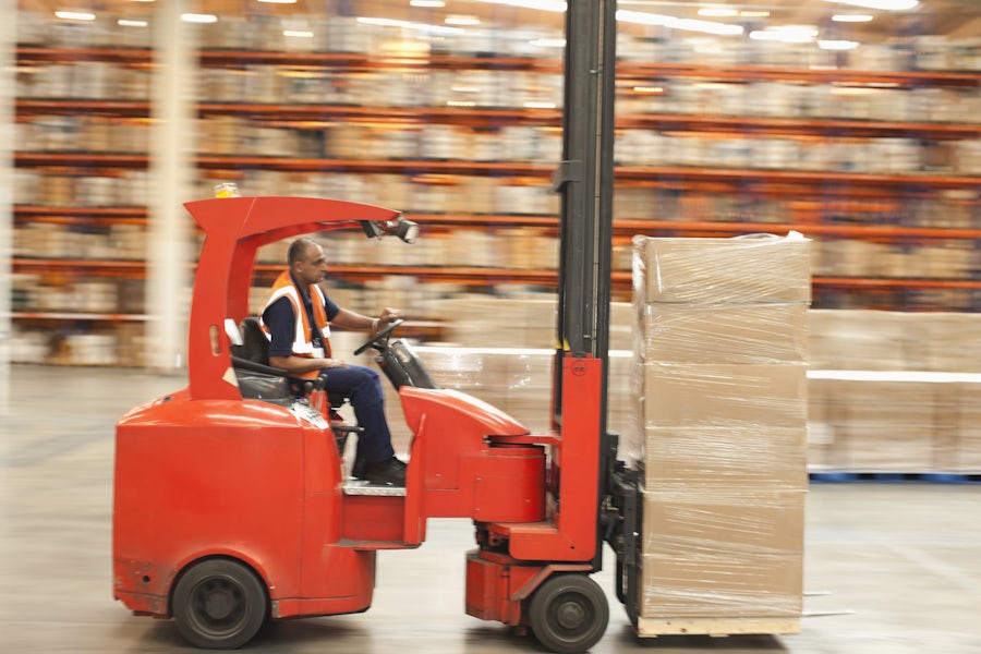 A worker moves boxes on an orange forklift in a warehouse