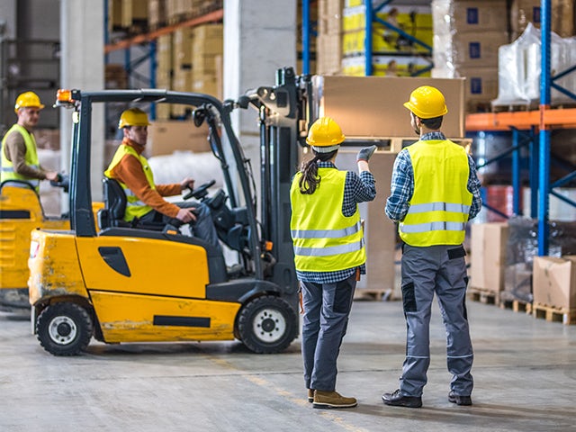 A group of workers in hardhats and reflective vests moving items in a warehouse