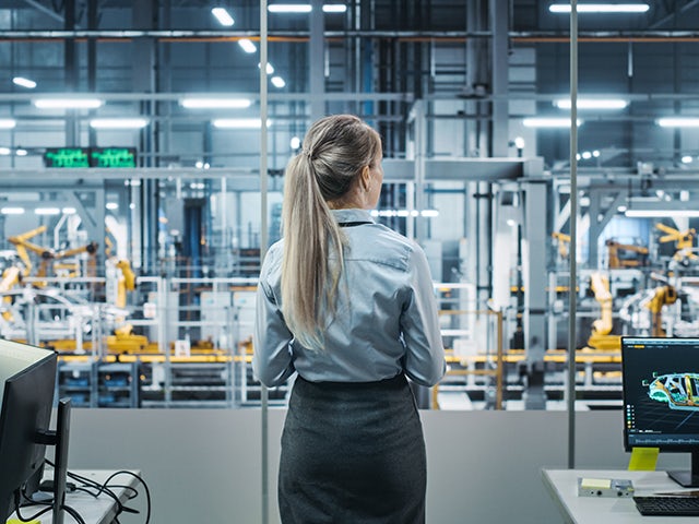 Female engineer standing in front of a factory assembly line.
