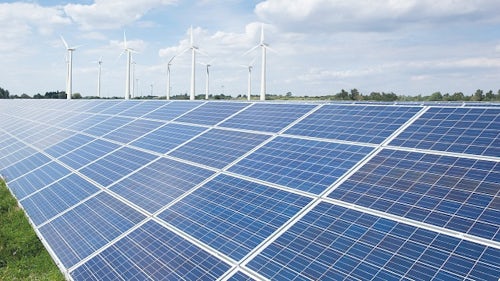 Solarmodule und Windkraftanlagen auf einer grünen Wiese.
