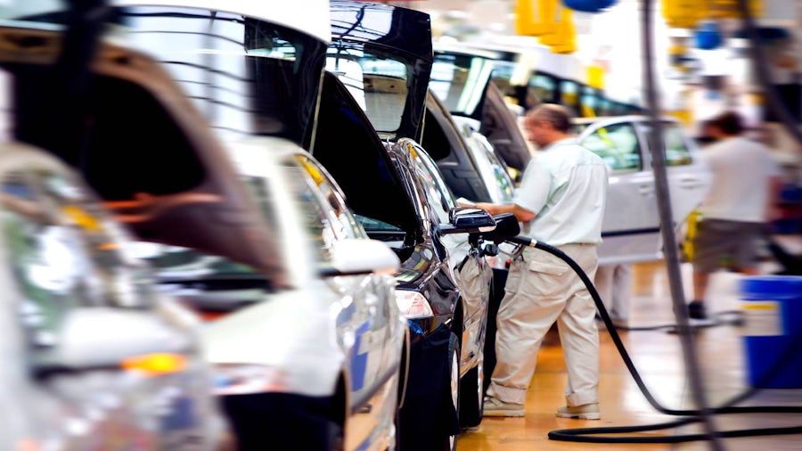 Automotive assembly line with workers inspecting vehicles and equipment during production.