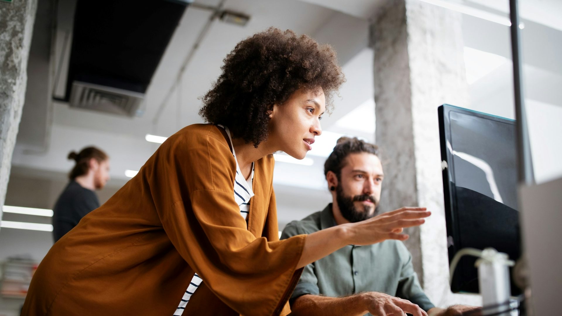 A man in an office working on a computer and a woman looking and pointing at the screen.