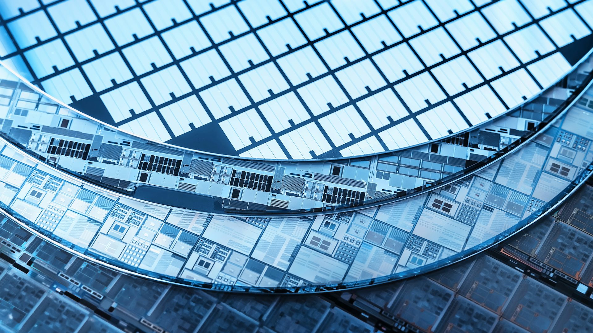 Close-up view of semiconductor wafers with intricate circuit patterns, featuring blue-toned reflective surfaces and detailed microchip designs.