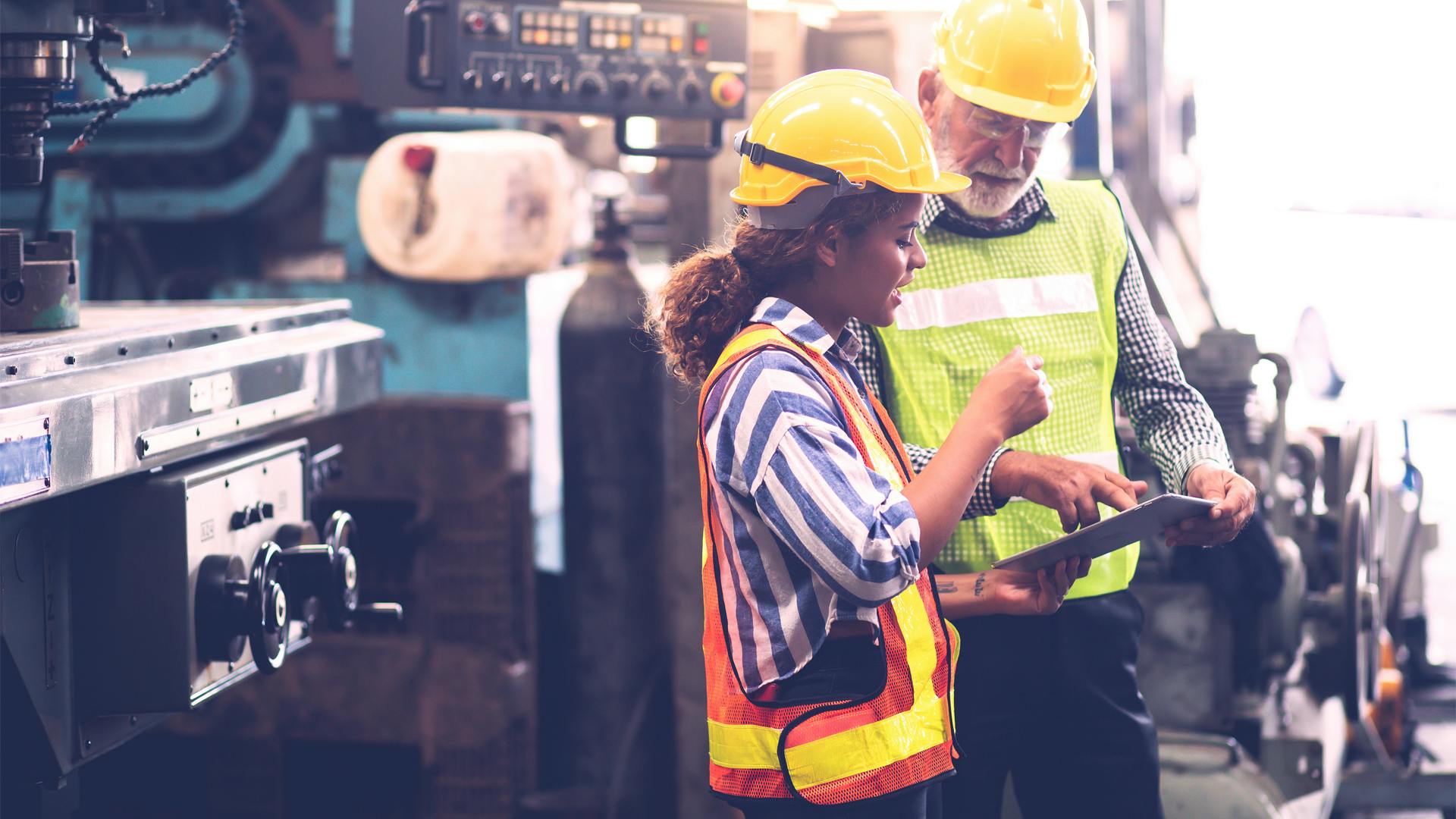 Two engineers use service lifecycle analytics software on a factory floor to maintain industrial machines.