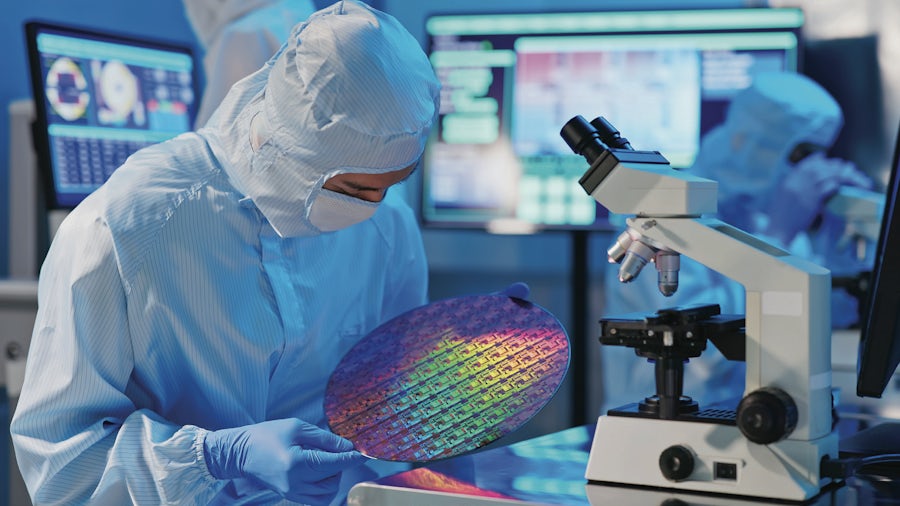 Image of a lab worker examining a semiconductor wafer fab.