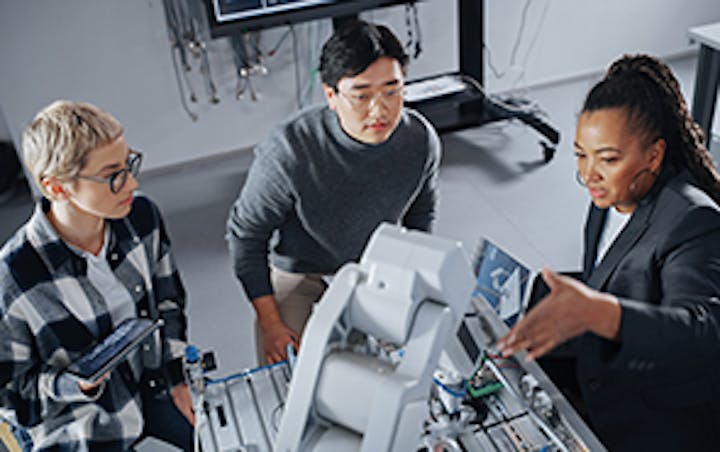 Drei Studenten umringen einen Roboterarm.