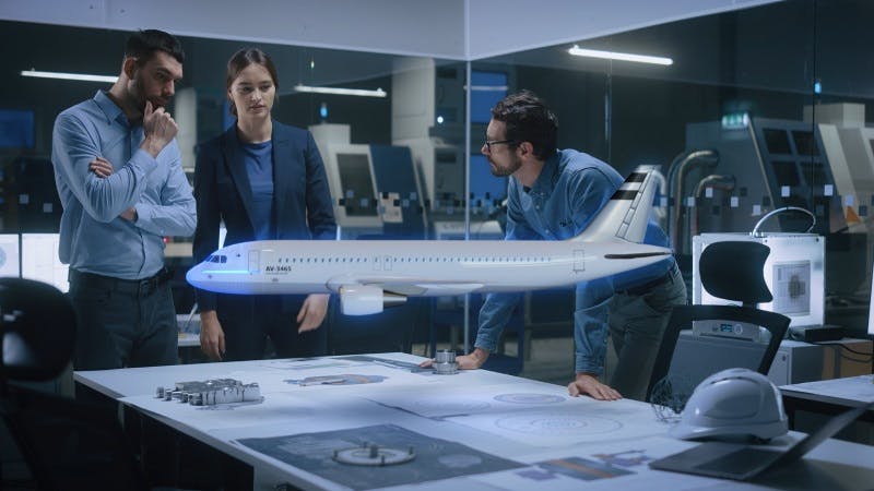 Three people in an office reviewing aerospace technical documents with a model of an airplane over the workstation.