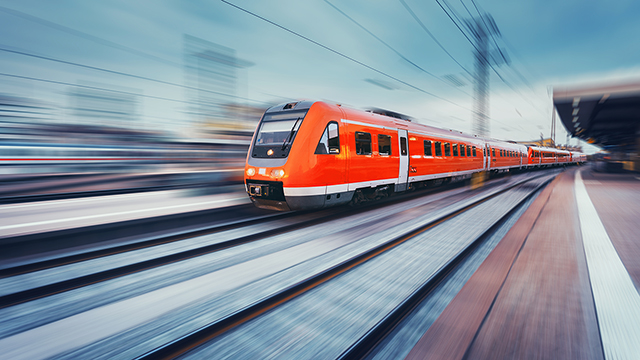 Modern red high-speed commuter train moving along a railway platform.